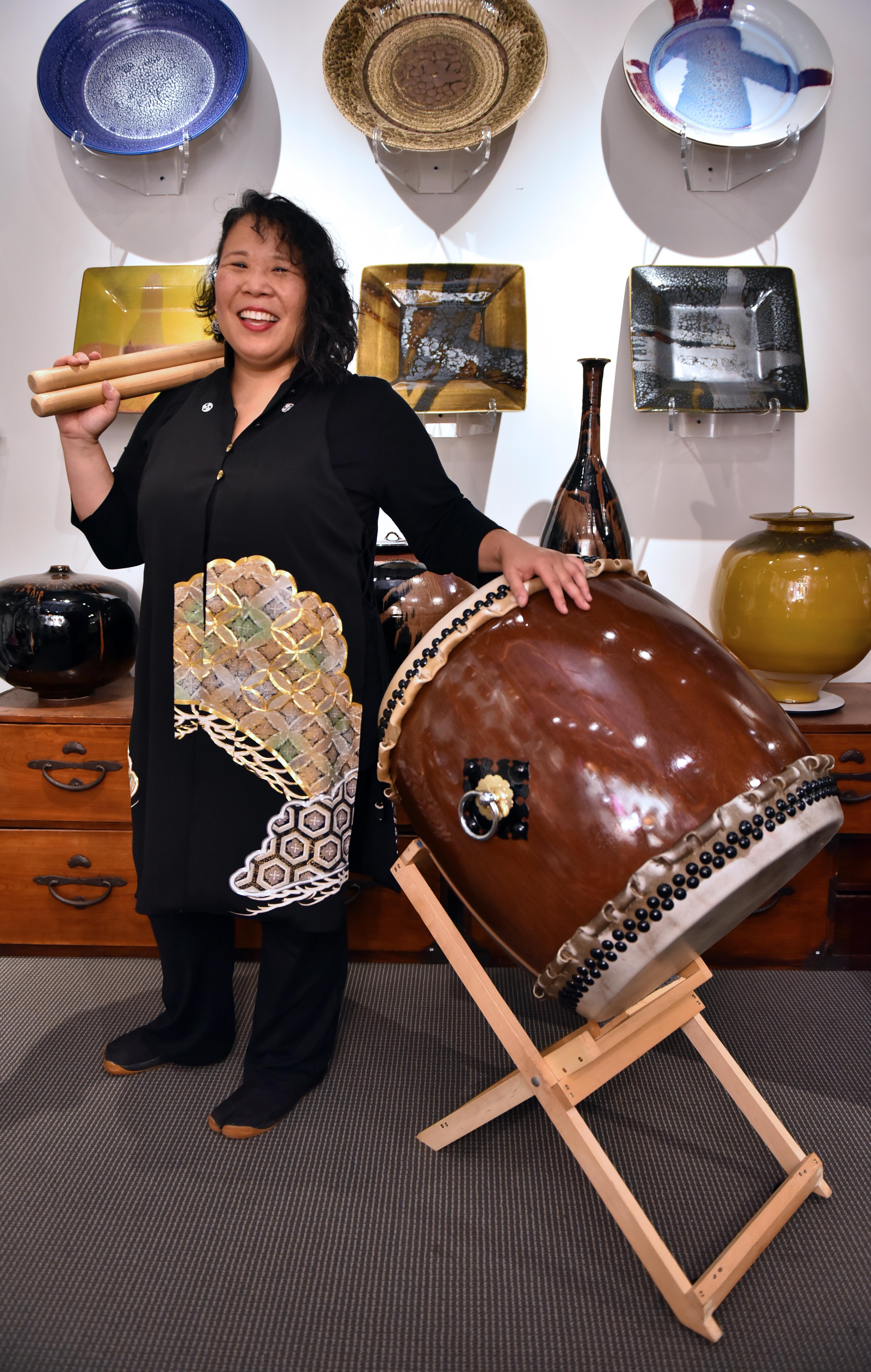 Karen Young wears a black shirt and holds taiko drum sticks in one hand. Her other hand is resting on a Japanese taiko drum.