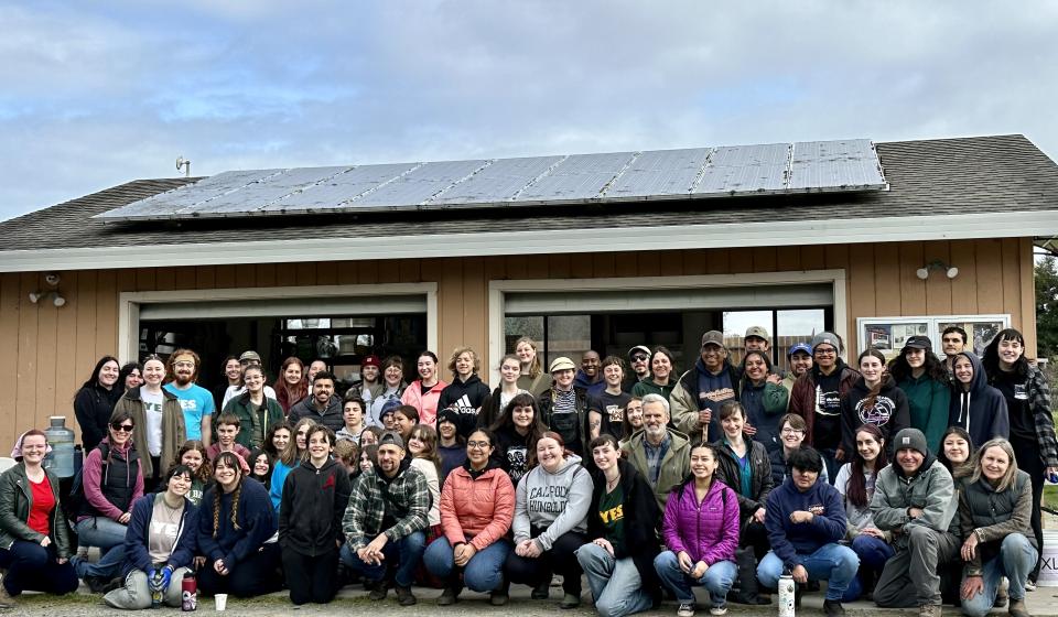 Large group of volunteers gather in front of the Potawot kitchen and shed (Spring 2023)
